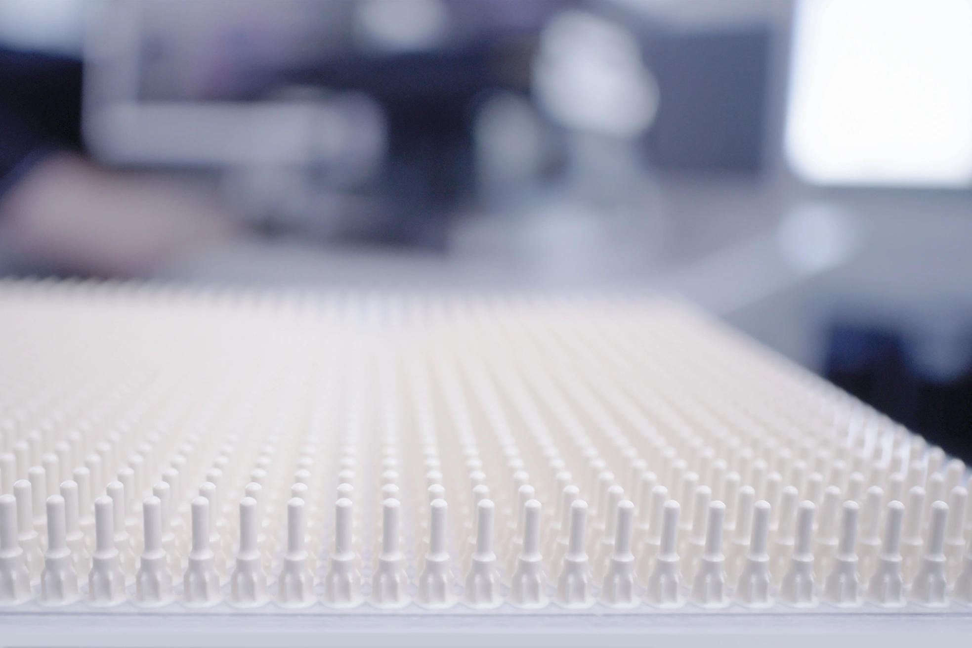 Close-up of a tray with multiple rows of white 3d printed ceramic needles.