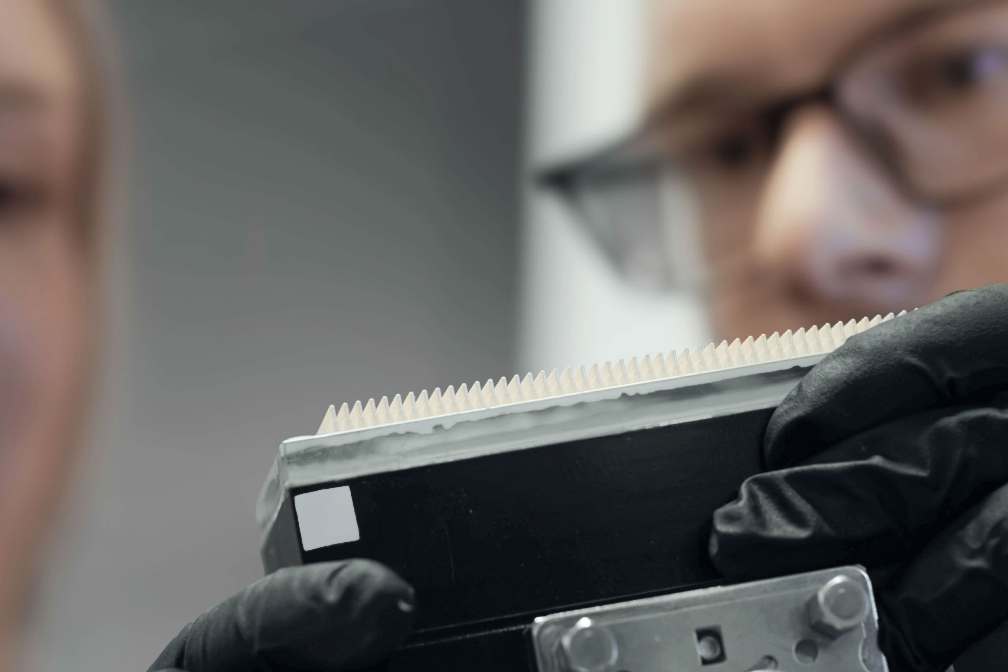 Person holding a black device with white small 3d printed ceramic needles, examining it closely.