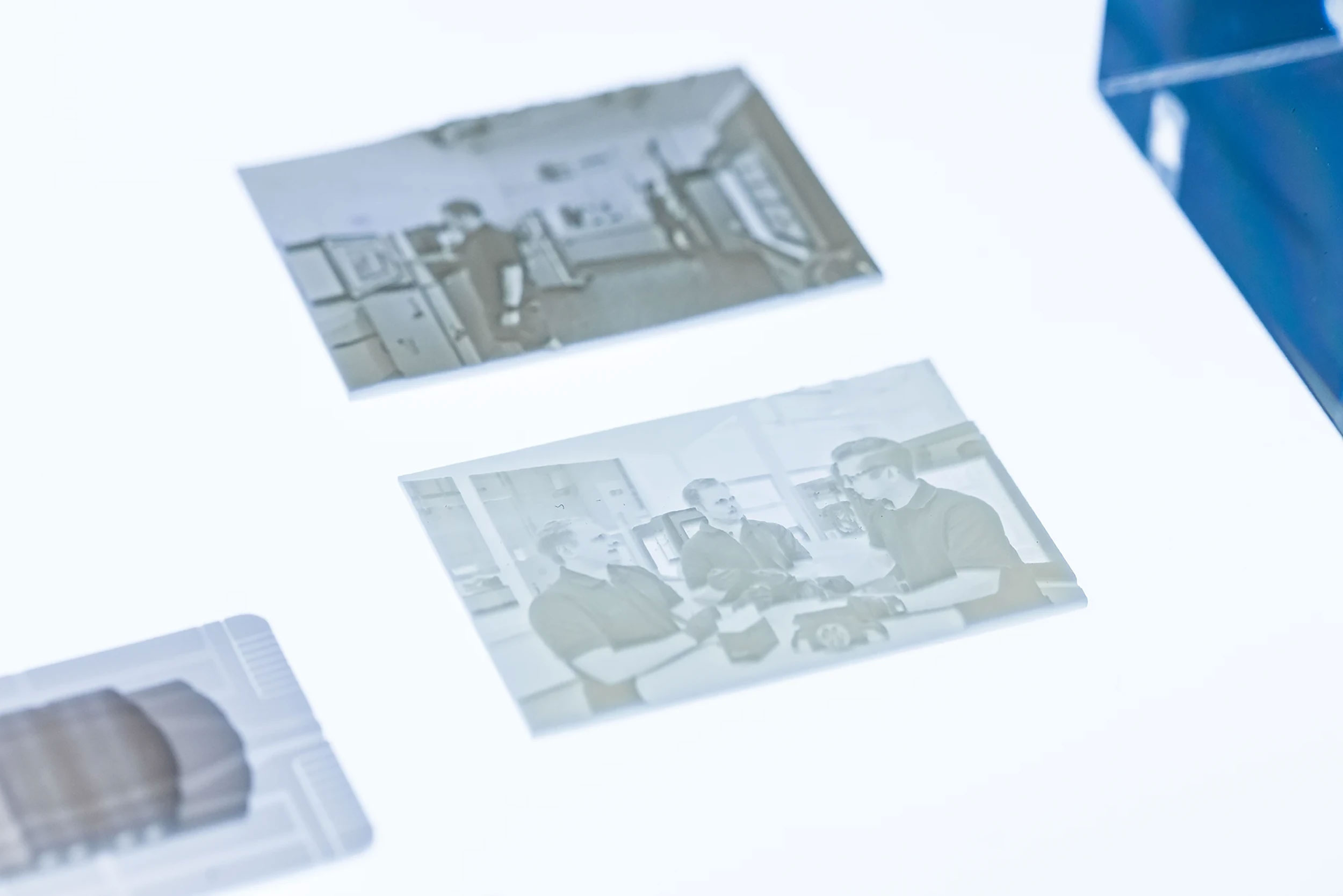 Photographic negatives showing a man working in an office and three men discussing a model car at a table.