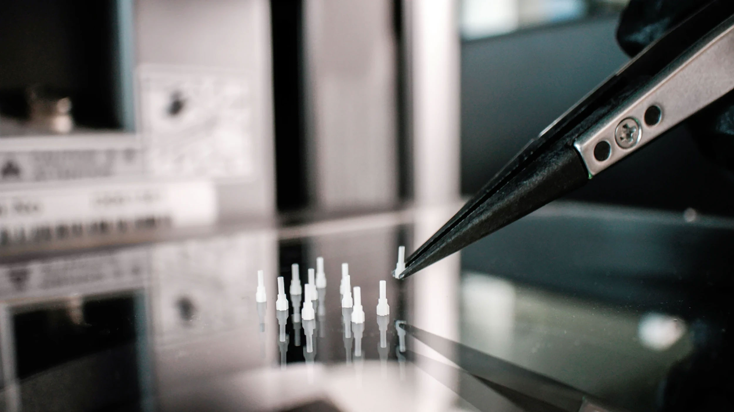 Tweezers holding a small white 3d printed ceramic object with multiple similar pins placed on it.