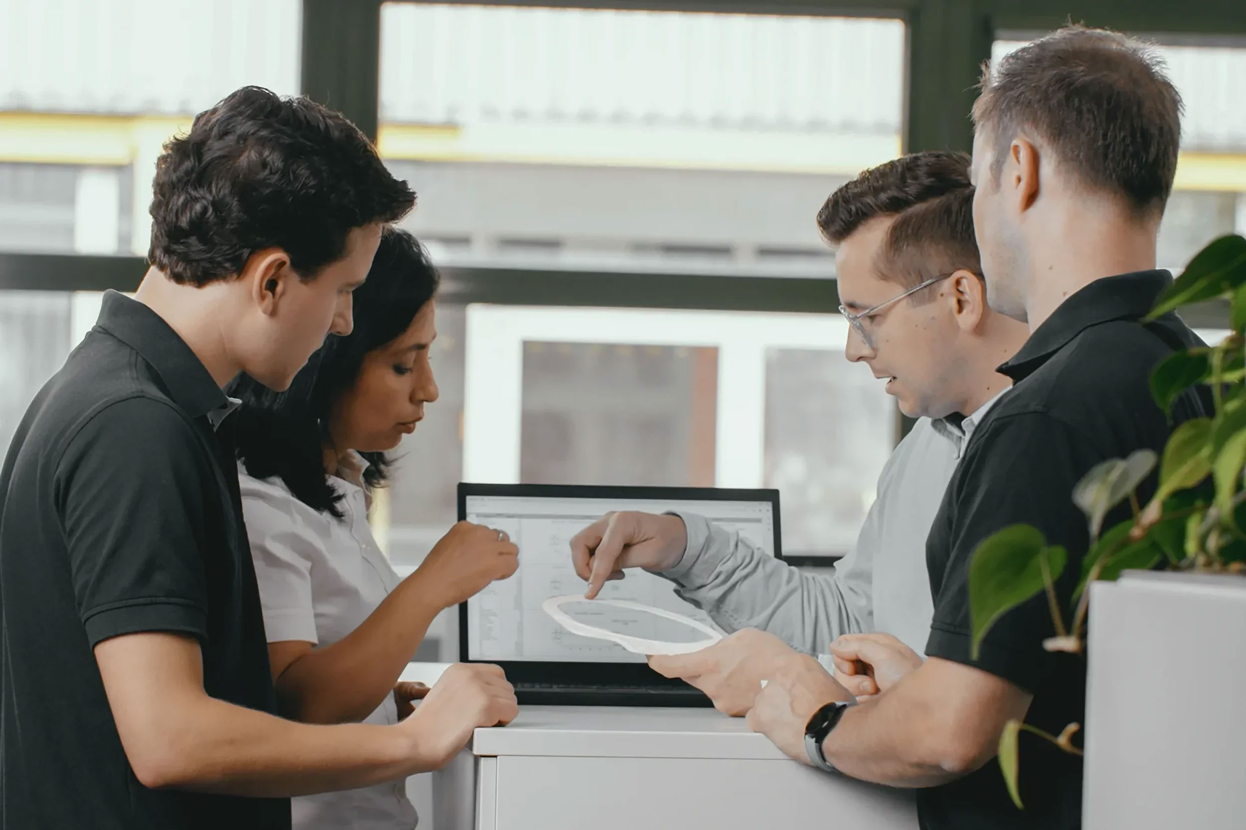 Four colleagues discussing a project with a laptop and a 3d printed ceramic object in an office setting.